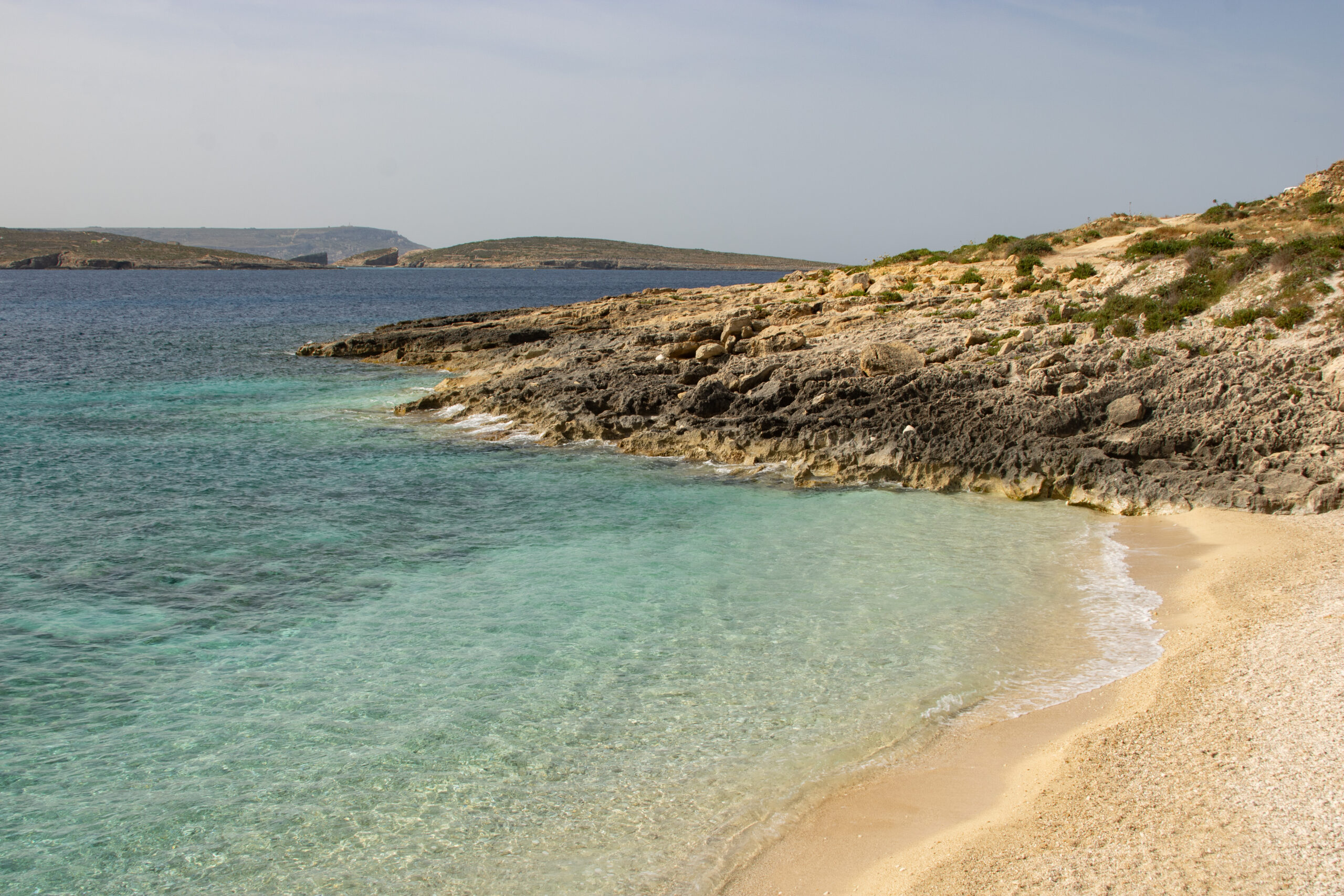 A beach with white sand and the sea views with Comino island in the background